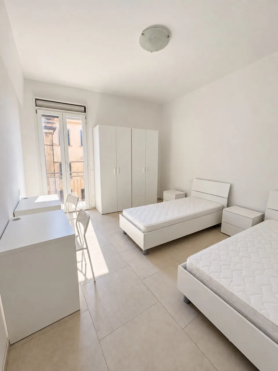 Camera doppia – Camera con due letti, armadio, scrivania e finestre sul balcone.