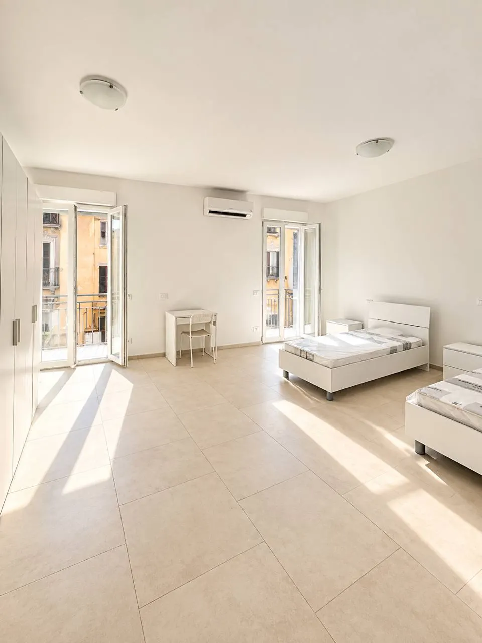 Spazio abitativo – Ambiente con due letti, armadio, scrivanie e accesso al balcone.