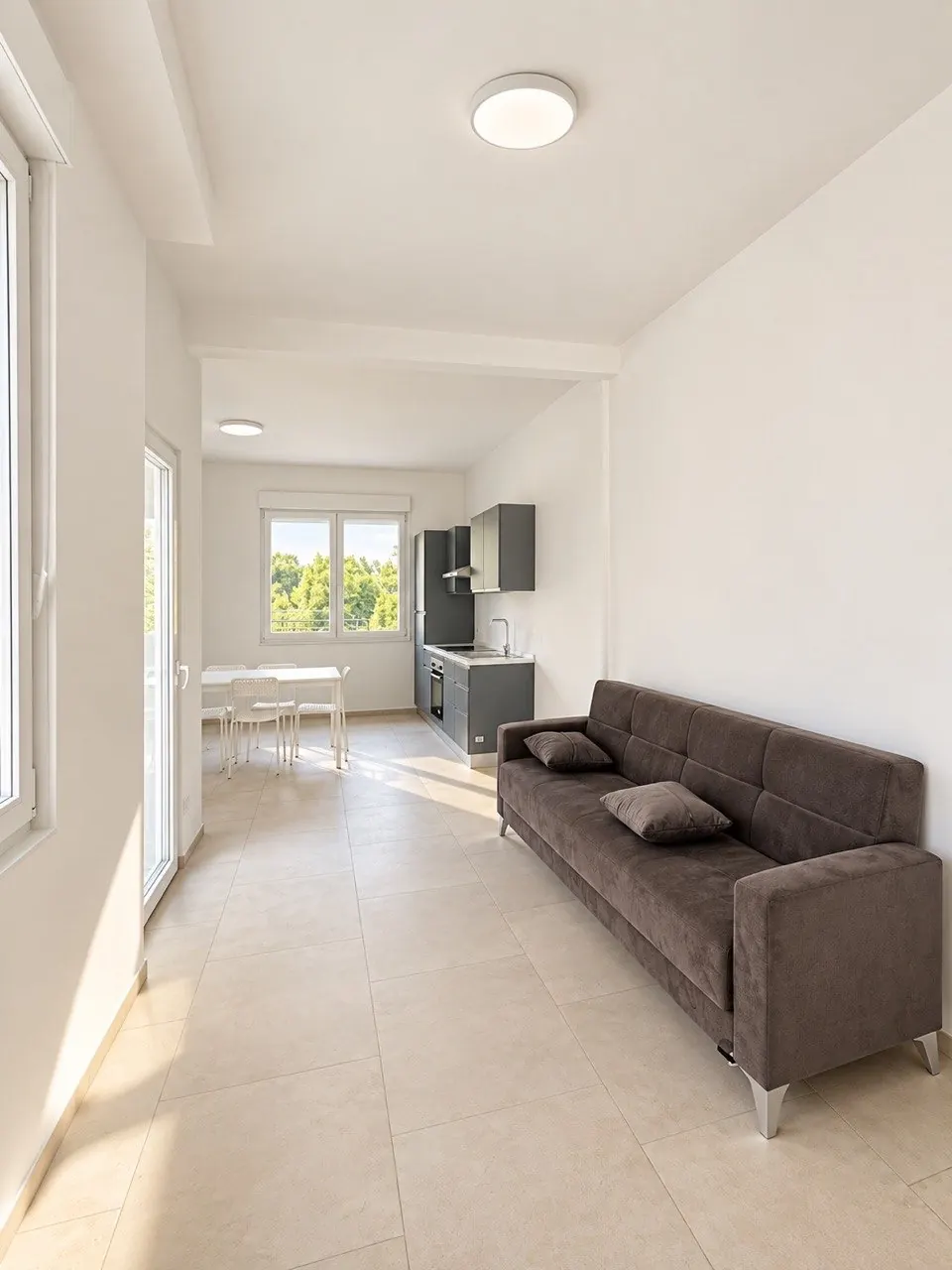 Zona giorno – Ambiente con divano, cucina sullo sfondo e accesso al balcone.