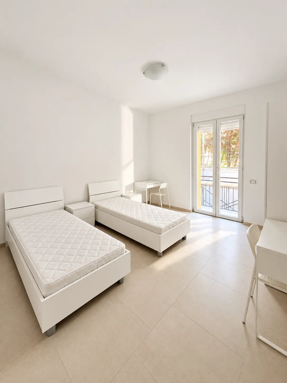 Spazio abitativo – Ambiente con due letti, comodini e scrivania.
